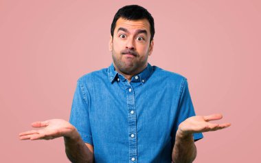 Yakışıklı adam mavi gömlek şüpheleri ve pembe bir arka plan üzerinde karıştırmayın yüz ifadesi ile