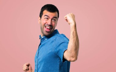 Pembe bir arka plan üzerinde bir zafer kutluyor mavi gömlek ile yakışıklı adam