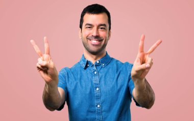 Gülümseyen ve zafer işareti, pembe arka plan gösteren mavi gömlek ile yakışıklı adam