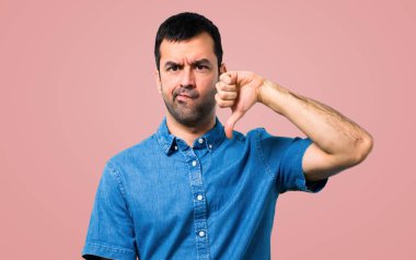 Başparmak aşağı negatif ifade işaretiyle gösterilen pembe arka plan mavi gömlek ile yakışıklı adam