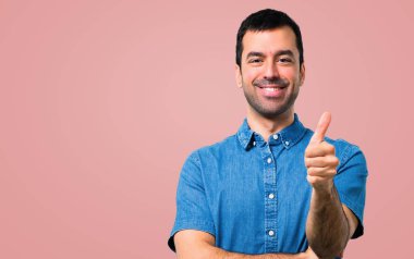 Jest Yaşasın vererek ve pembe arka plan gülümseyen mavi gömlek ile yakışıklı adam