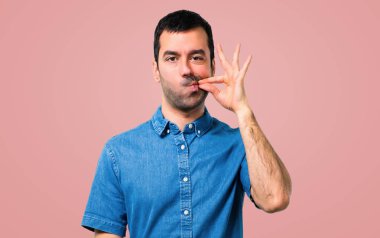 Ağız ve sessizlik bir jest pembe bir arka plan üzerinde kapanış bir işaret gösteren mavi gömlek ile yakışıklı adam