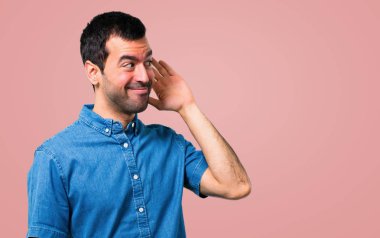 Mavi gömlek pembe bir arka plan üzerinde bir şey dinleme ile yakışıklı adam