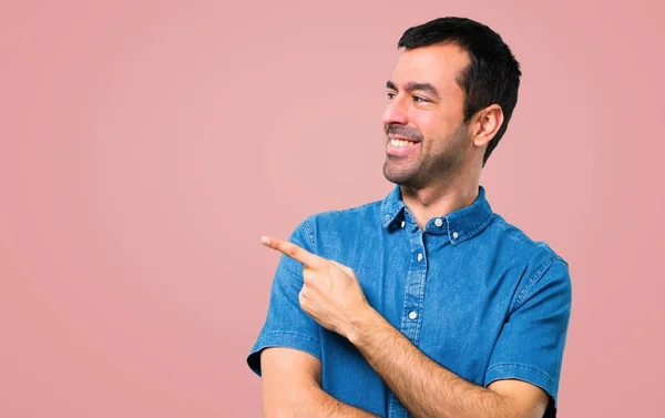 英俊的男人与蓝色衬衫手指指向一侧 并提出在粉红色的背景产品 — 图库照片