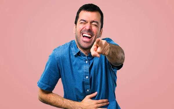 誰かに指で指しているとたくさん笑って ピンクの背景に青いシャツでハンサムな男 — ストック写真