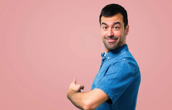 英俊的男人与蓝色衬衫指向后面与食指在粉红色的背景 — 图库照片
