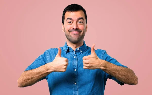 青いシャツ ジェスチャー親指を与えるとピンク背景に笑顔でハンサムな男 — ストック写真