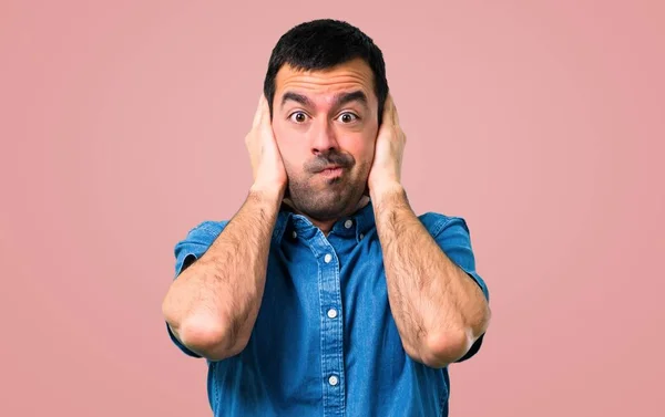 英俊的人与蓝色衬衫覆盖两个耳朵与手在粉红色的背景 — 图库照片