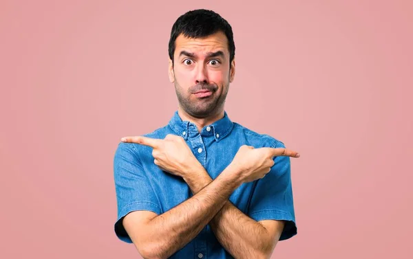 ピンクの背景に疑問を持つ根を指している青いシャツとハンサムな男 — ストック写真