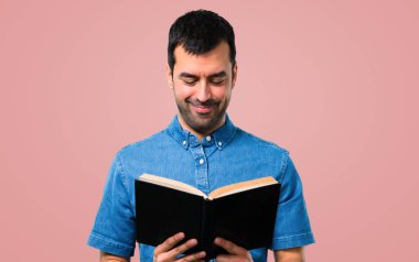 Mavi gömlek pembe bir arka plan üzerine bir kitap okuma ile yakışıklı adam