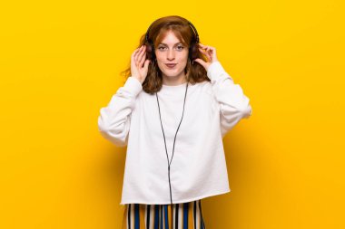 Sarı duvar kulaklık ile müzik dinlemek genç Kızıl saçlı kadın