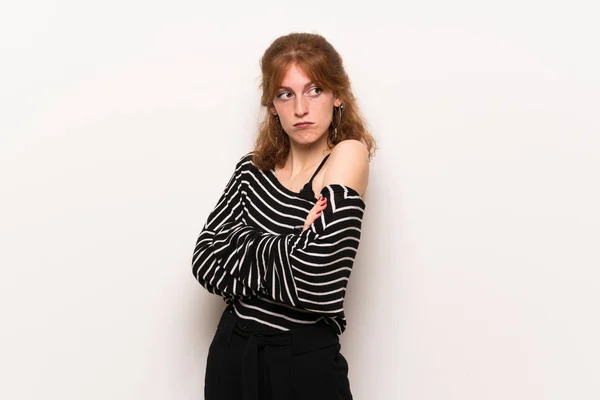 Young redhead woman over white wall making doubts gesture while lifting the shoulders
