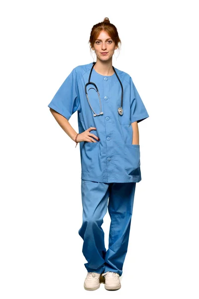 ヒップで腕とポーズと分離の白い背景の上に笑顔赤毛の若い看護婦のフルレングス ショット — ストック写真