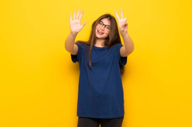 Yedi parmak ile sayma sarı duvarın üzerinden gözlüklü genç kadın