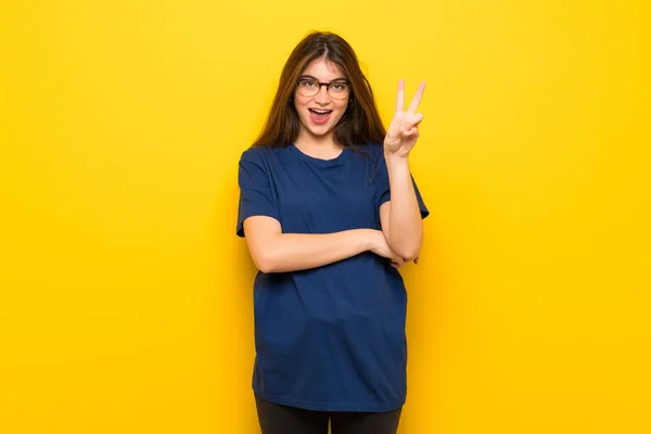 Gülümseyen Zafer Işaret Gösteren Sarı Duvarın Üzerinden Gözlüklü Genç Kadın — Stok fotoğraf