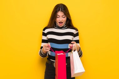 Sarı duvar bir sürü alışveriş torbaları tutarken sürpriz genç kadın