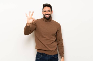 Beyaz duvar mutlu ve sayım üç parmak ile yakışıklı adam