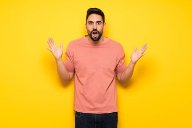 Sürpriz ve şok yüz ifadesi ile sarı duvarın üzerinden yakışıklı adam