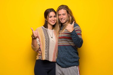 Hippi çift hareketi her iki el ile Yaşasın vererek ve gülümseyen sarı arka plan üzerinde