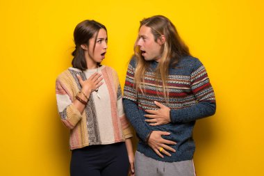 Hippi çift sürpriz ve şok yüz ifadesi ile sarı arka plan üzerinde