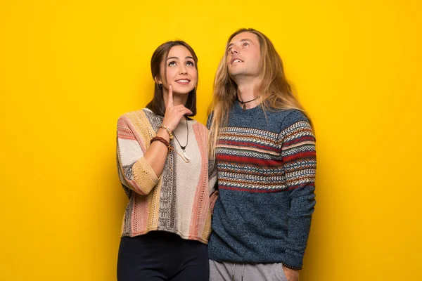 Hippie couple over yellow background thinking an idea while looking up