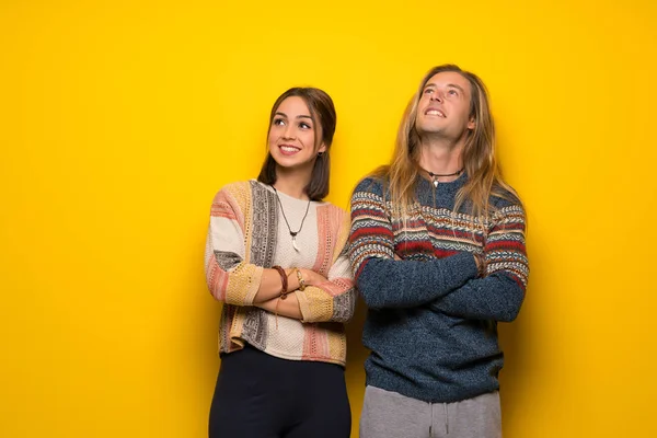 Hippie couple over yellow background looking up while smiling