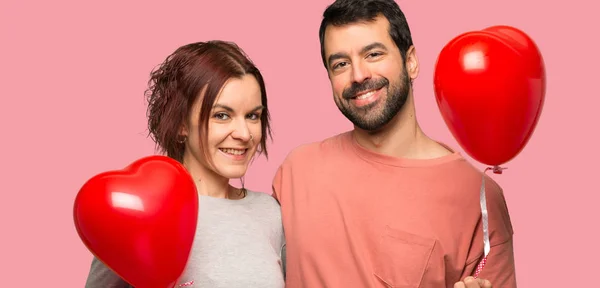 Couple in valentine day with balloons with heart shape over isolated pink background