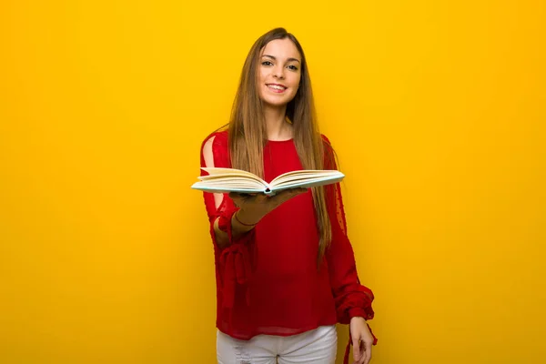 Jovem Com Vestido Vermelho Sobre Parede Amarela Segurando Livro Dando — Fotografia de Stock