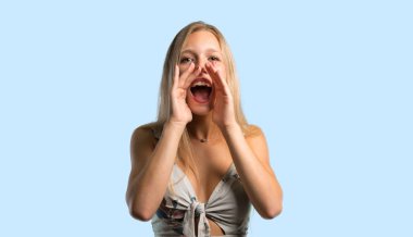 Geniş açık ağız ile bağırarak ve mavi arka plan üzerinde bir şey ilan sarışın genç kadın