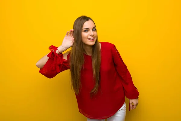 年轻的女孩与红色礼服在黄色的墙壁上听东西 把手放在耳朵上 — 图库照片