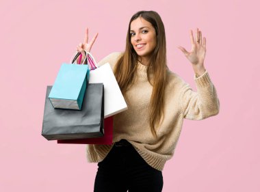 Alışveriş torbaları yedi ile izole pembe bir arka plan üzerinde parmak sayma ile genç kız