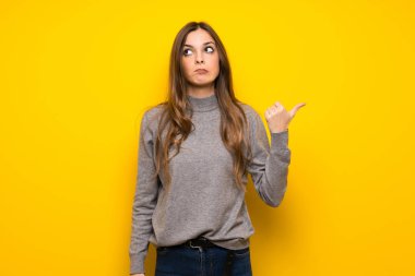 Genç kadın sarı duvar mutsuz ve tarafa işaretleme