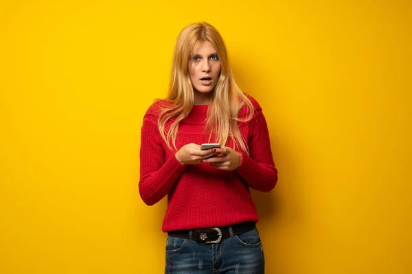 黄色の壁の携帯電話で音楽を聴く以上の金髪女性 — ストック写真