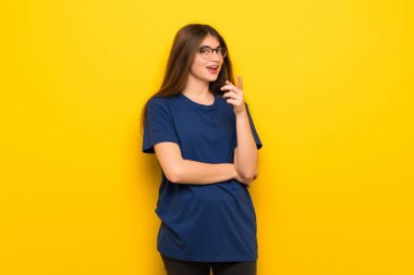Sarı duvarın üzerinden gözlüklü genç kadın seni kendinden emin bir ifade ile parmak işaret