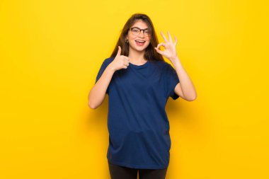 Sarı duvar gösteren ok işareti ile ve jest bir başparmak veren gözlüklü genç kadın