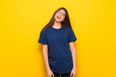 Dil komik göz olan kameraya gösterilen sarı duvarın üzerinden gözlüklü genç kadın