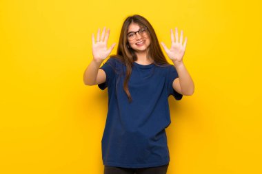 On parmak ile sayma sarı duvarın üzerinden gözlüklü genç kadın