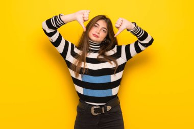 Başparmak aşağı her iki el ile gösterilen sarı duvarın üzerinden genç kadın