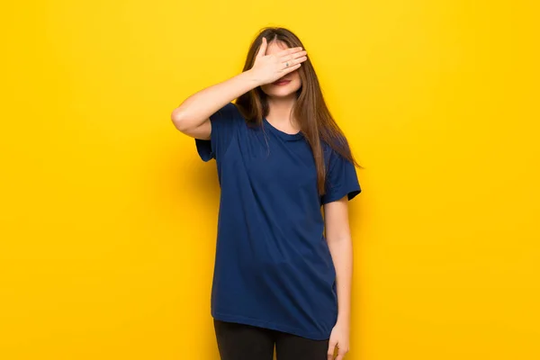 Young woman with glasses over yellow wall covering eyes by hands. Do not want to see something
