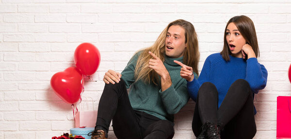 Couple in valentine day pointing finger to the side with a surprised face