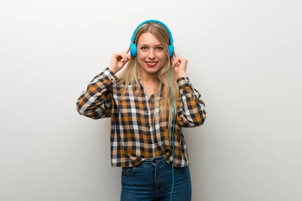 Sarışın Genç Kız Üzerinde Beyaz Duvar Kulaklık Ile Müzik Dinlemek — Stok fotoğraf