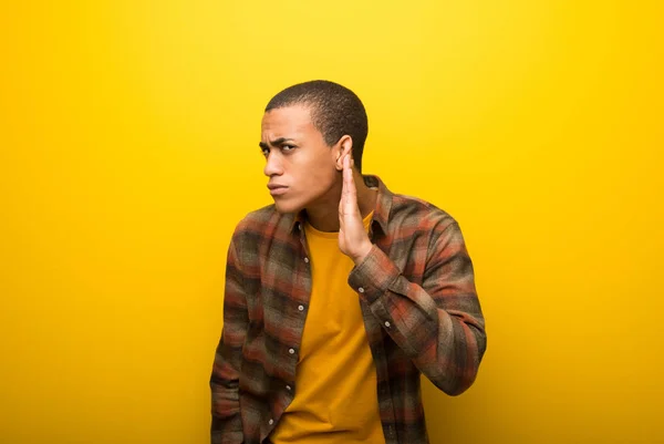 Giovane Uomo Afroamericano Sfondo Giallo Vibrante Ascoltando Qualcosa Mettendo Mano — Foto Stock