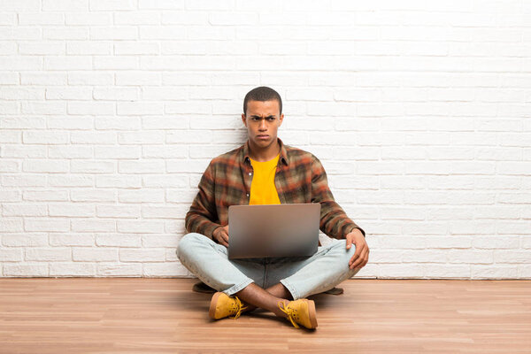 African american man sitting on the floor with his laptop feeling upset
