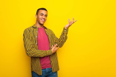 Genç afro Amerikalı adam ellerini yanına gelmek için davet için uzanan sarı zemin üzerine