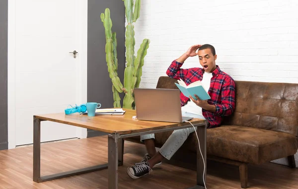 Africano Americano Com Laptop Sala Estar Segurando Livro Surpreendido Enquanto — Fotografia de Stock