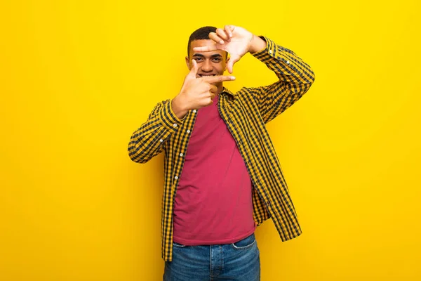 Young afro american man on yellow background focusing face. Framing symbol