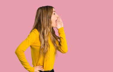 lateral izole pembe arka plan üzerine açık geniş ağızlı bağırmayı sarı kazaklı genç kız