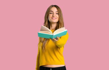 bir kitap ve birileriyle izole pembe arka plan veren sarı kazaklı genç kız