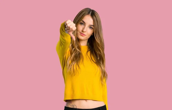 分離ピンク背景に親指で下を負の式と記号を示す黄色のセーターを持つ少女 — ストック写真
