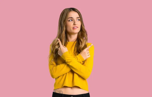 Fiatal Lány Kétségek Elszigetelt Rózsaszín Háttér Elágazásán Mutat Sárga Pulóver — Stock Fotó